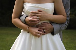 Close-up shot of embracing hands with wedding rings against a white dress.