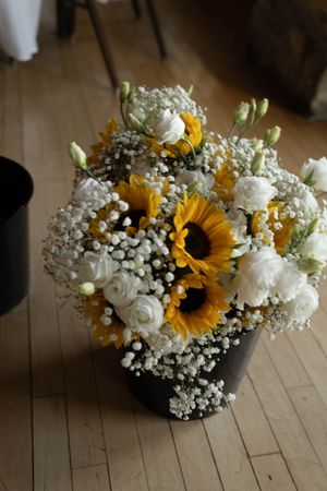 Wedding bouquet featuring sunflowers, white roses, and baby's breath on wooden flooring.