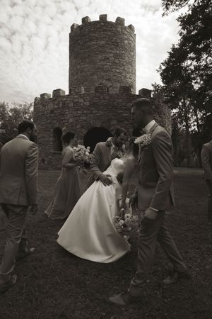 Wedding party posing in front of a historic stone tower in black and white.