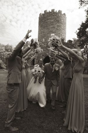 Fun wedding party poses playfully in black and white near historic stone tower.