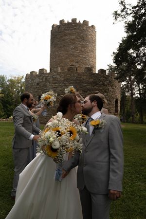 Wedding party sharing celebratory moments with sunflower bouquets by stone castle tower.