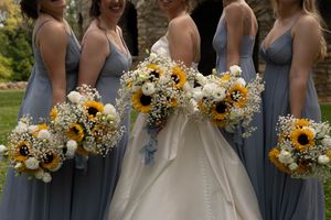 Wedding group stands together with yellow and white bouquets against rustic backdrop.