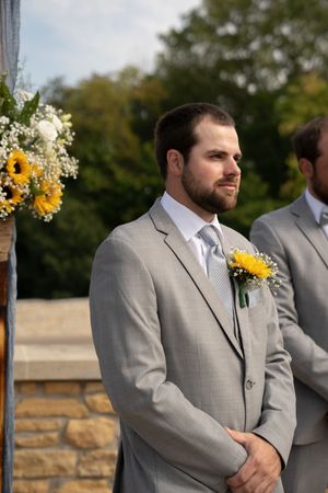 Groomsmen in gray suits with sunflower boutonnieres standing at ceremony.