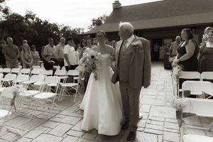 Wedding ceremony guests seated in white chairs on a stone patio during an outdoor celebration.