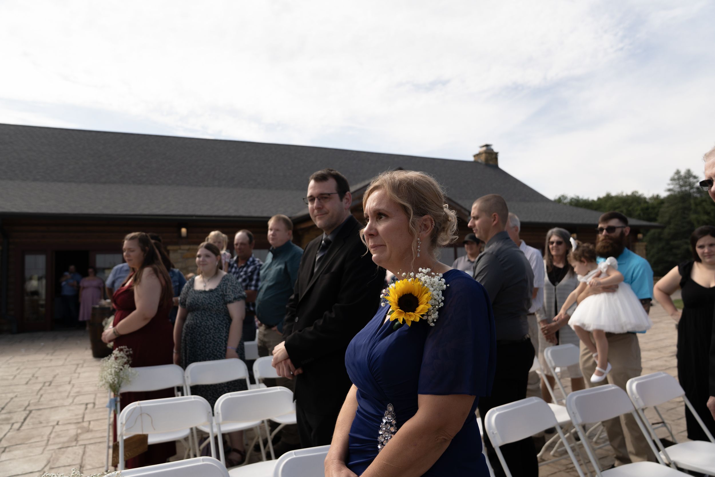 Guests gather for an outdoor wedding ceremony with white chairs arranged on a stone patio.