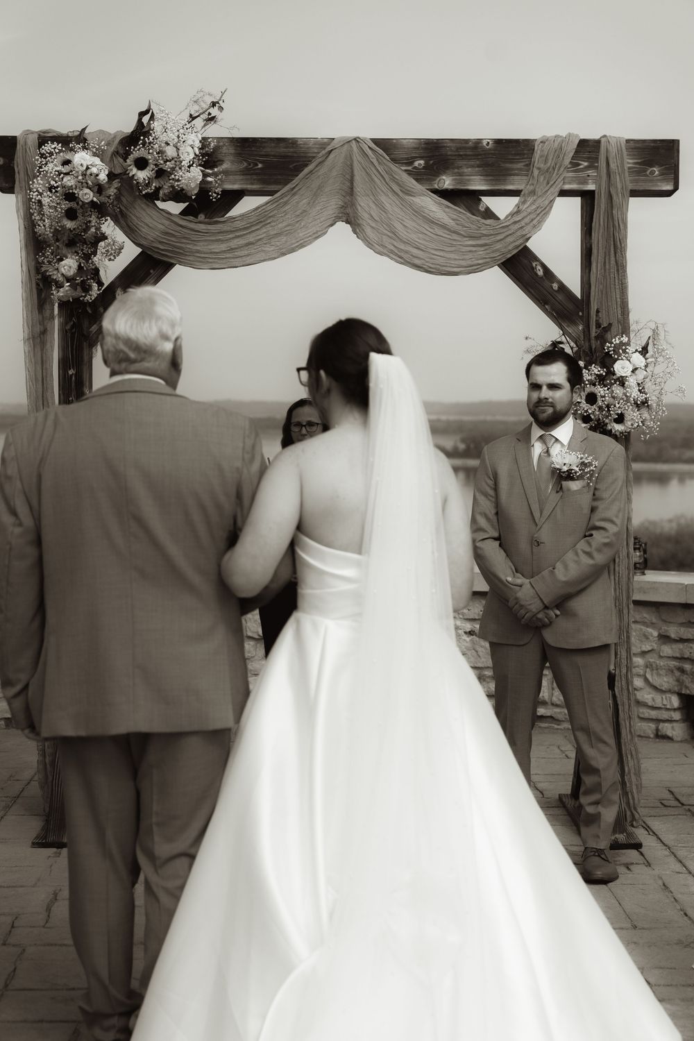 Wedding ceremony at scenic overlook with wooden arch and draped fabric decor.