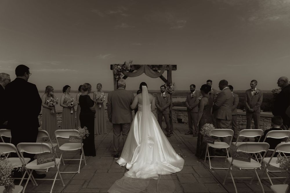 Black and white photo of outdoor wedding ceremony with guests seated at scenic venue.