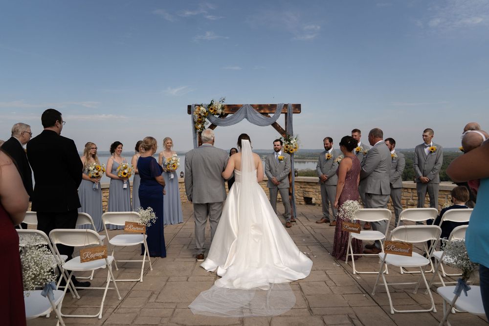 Outdoor wedding ceremony with wooden arch and white draping overlooking scenic landscape.