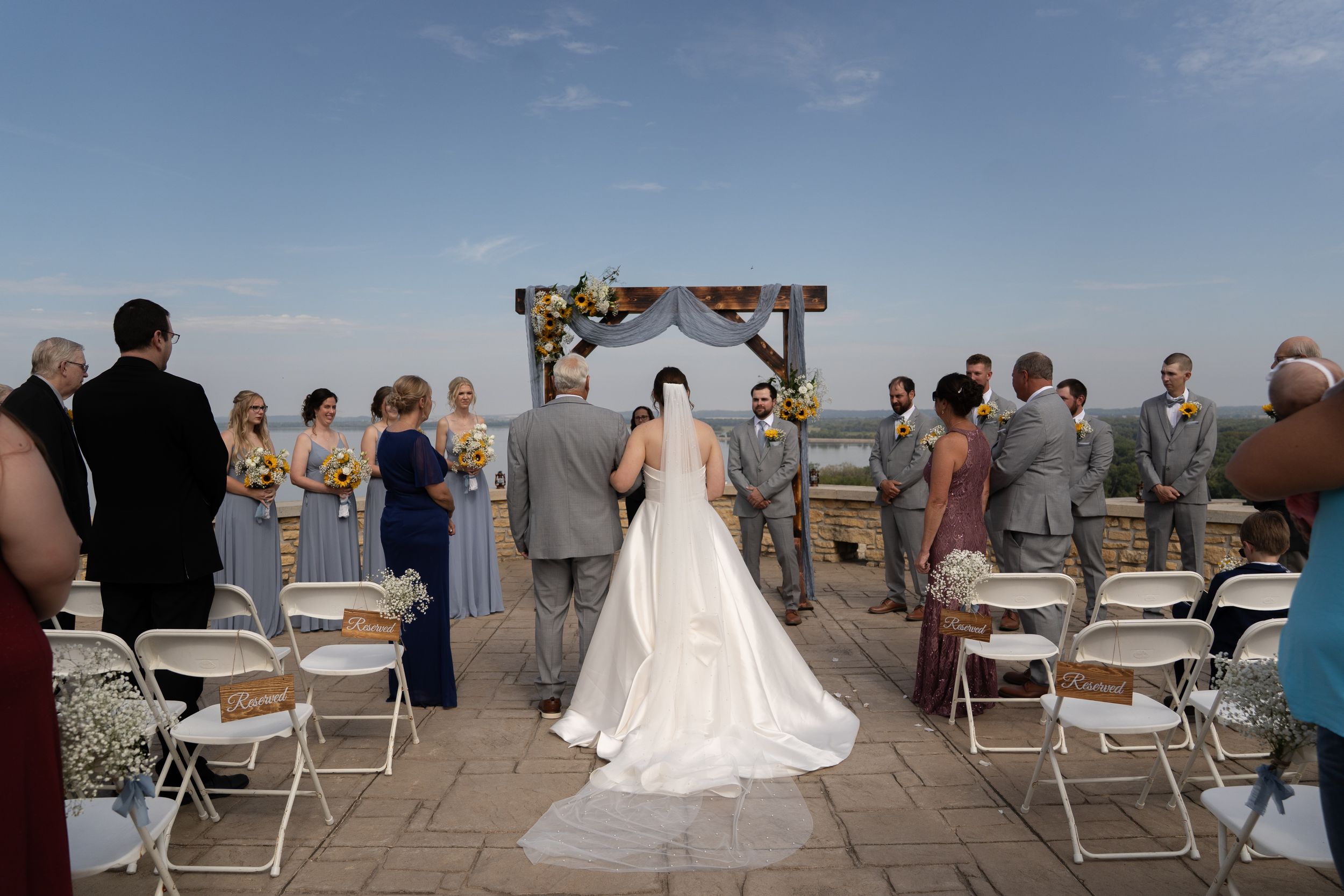 Outdoor wedding ceremony with wooden arch and white draping overlooking scenic landscape.
