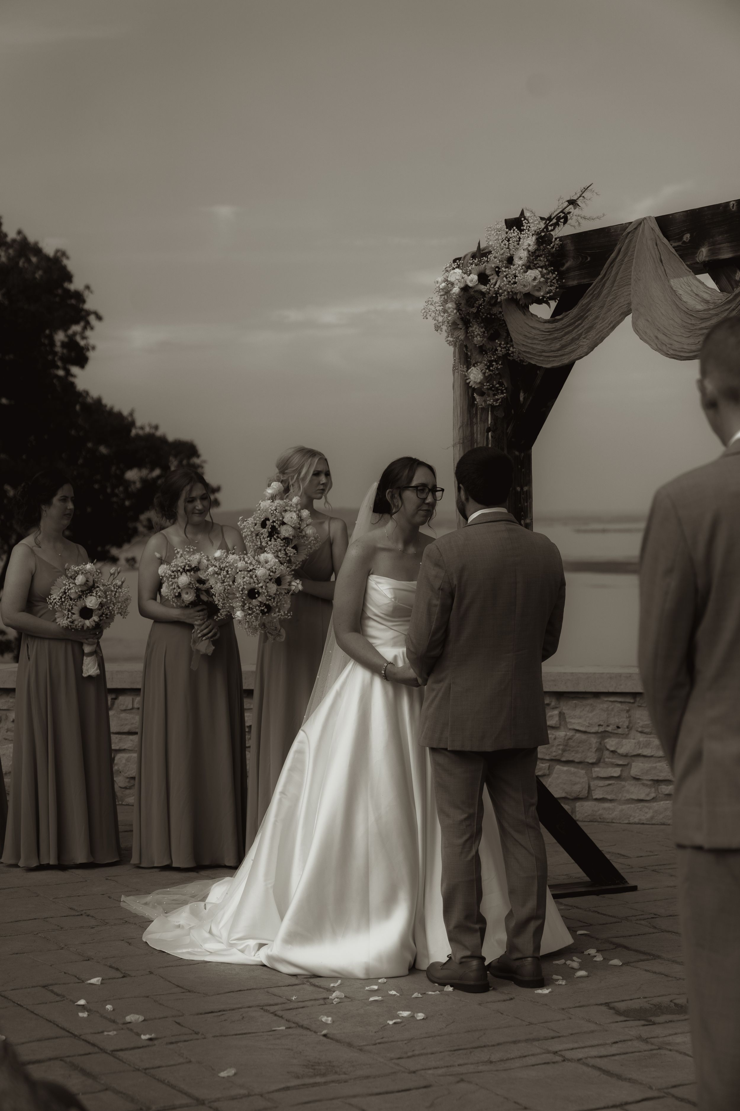 Black and white photo of wedding ceremony on stone patio with bridal party in formal attire.