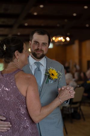 Couple dancing in formal attire with sunflower boutonniere at indoor reception.
