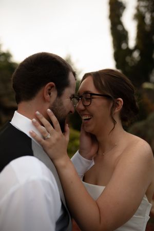 Intimate wedding portrait showing joyful laughter and tender touch against a natural backdrop.
