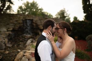 Intimate wedding moment captured against rustic stone wall with water feature.