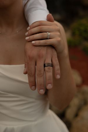 Close-up of newlywed hands showing wedding rings against white dress fabric.
