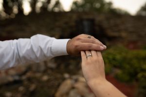 Close-up of hands with wedding rings against stone wall background.