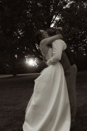 A romantic couple dancing outdoors at sunset with the bride's white dress flowing in silhouette.