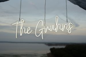 Illuminated neon wedding sign mounted on wooden beams against sunset sky.