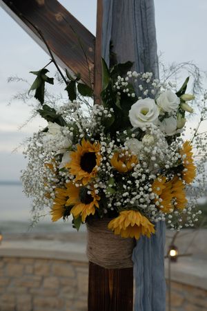 Floral wedding arch decoration featuring sunflowers, white roses and baby's breath in rustic setting.