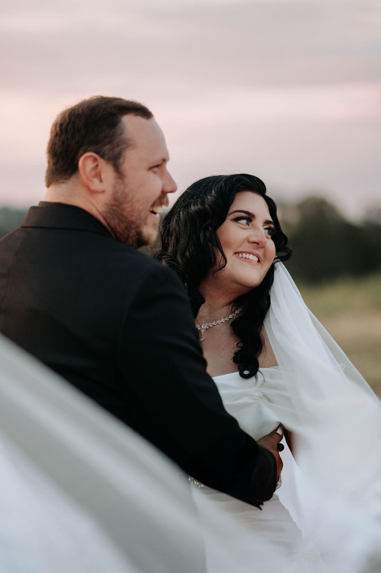 A romantic wedding portrait series shows a couple embracing outdoors at sunset with the bride's veil flowing in the breeze.