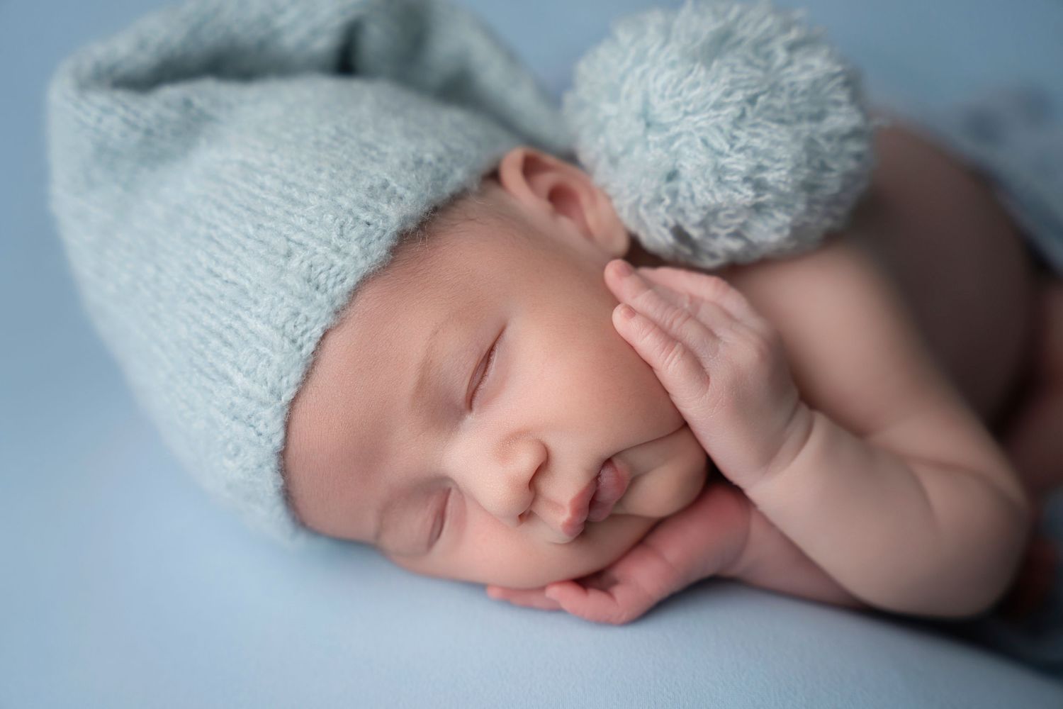 Miami Maternity photographer A sleeping newborn baby wearing a knit hat lies peacefully on a soft blanket.