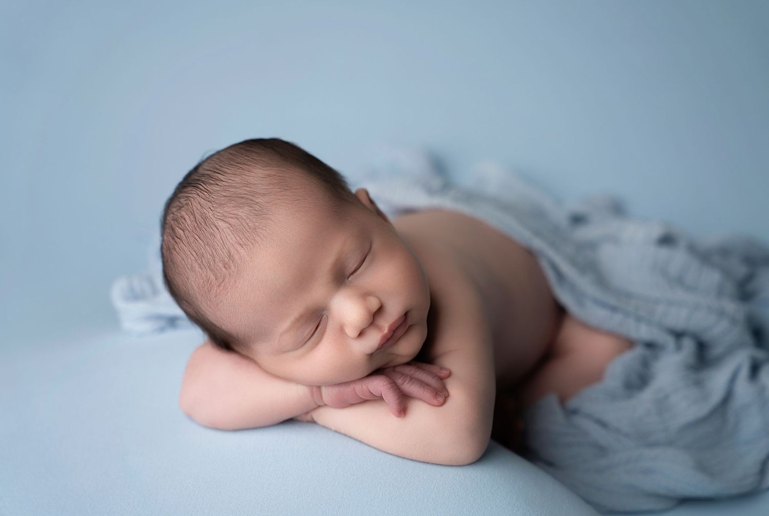 Miami Maternity photographer A peaceful newborn baby sleeps on soft gray fabric in a gentle curled position during a photo session.
