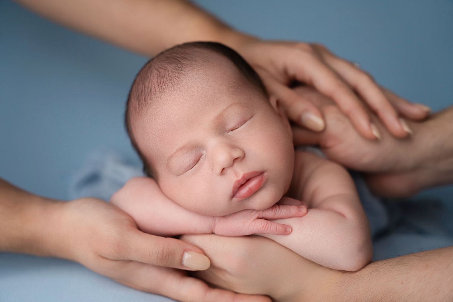 Miami Maternity photographer Peaceful sleeping newborn cradled gently in adult hands against soft blue background.