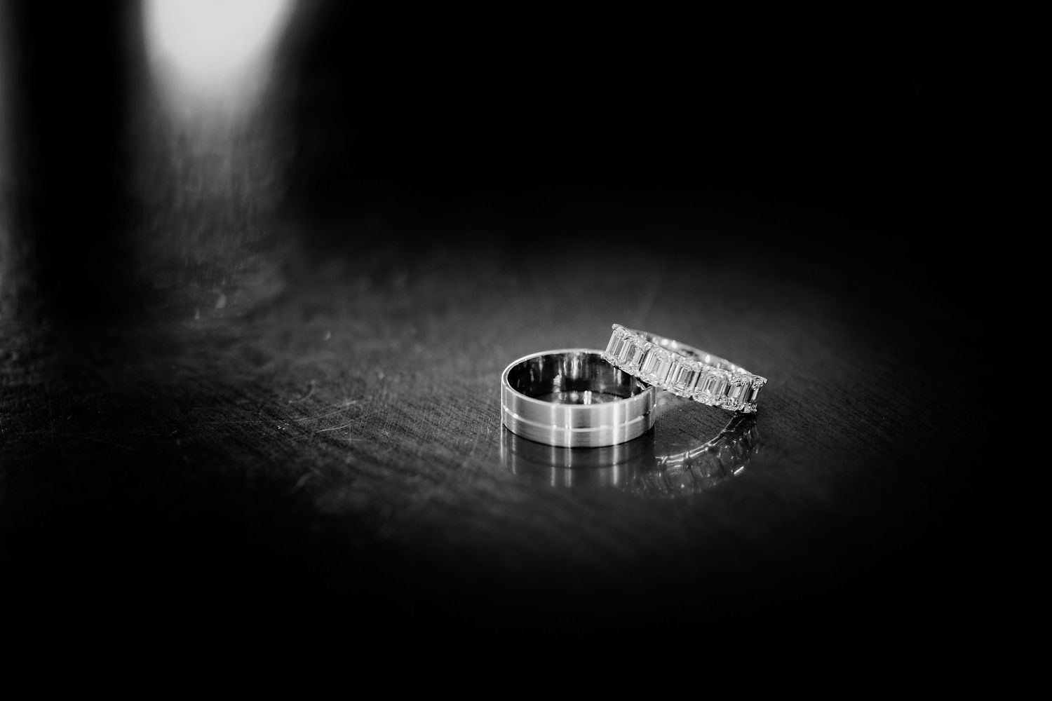 Two wedding rings in black and white with dramatic lighting on a textured surface.