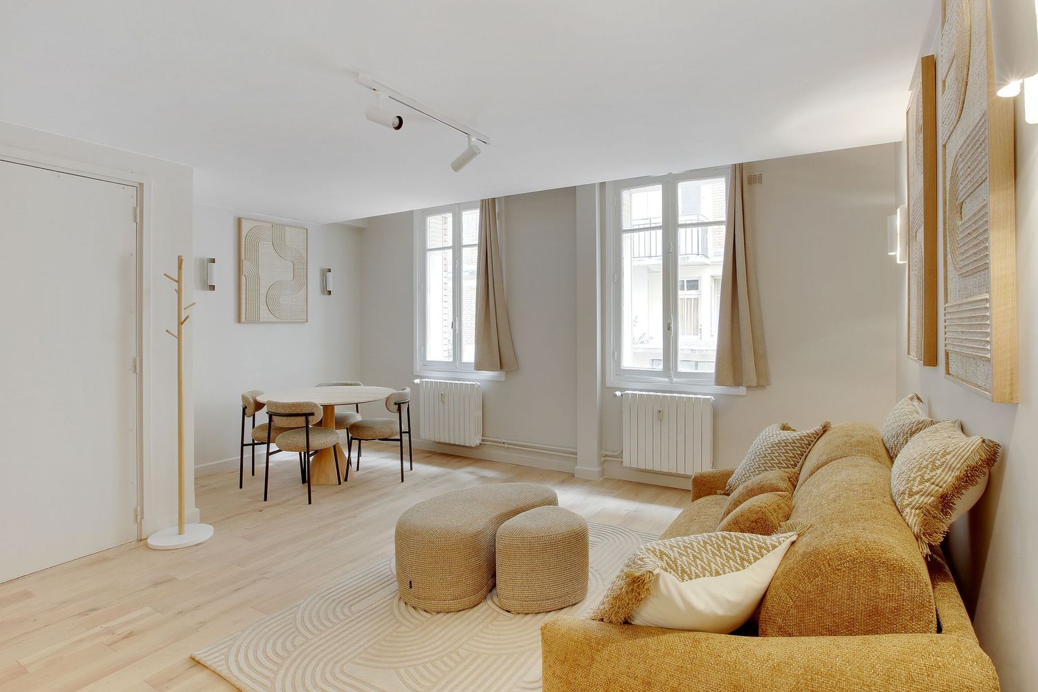 Bright Parisian apartment living room with mustard sofa, wooden floor, and dining area by tall windows.
