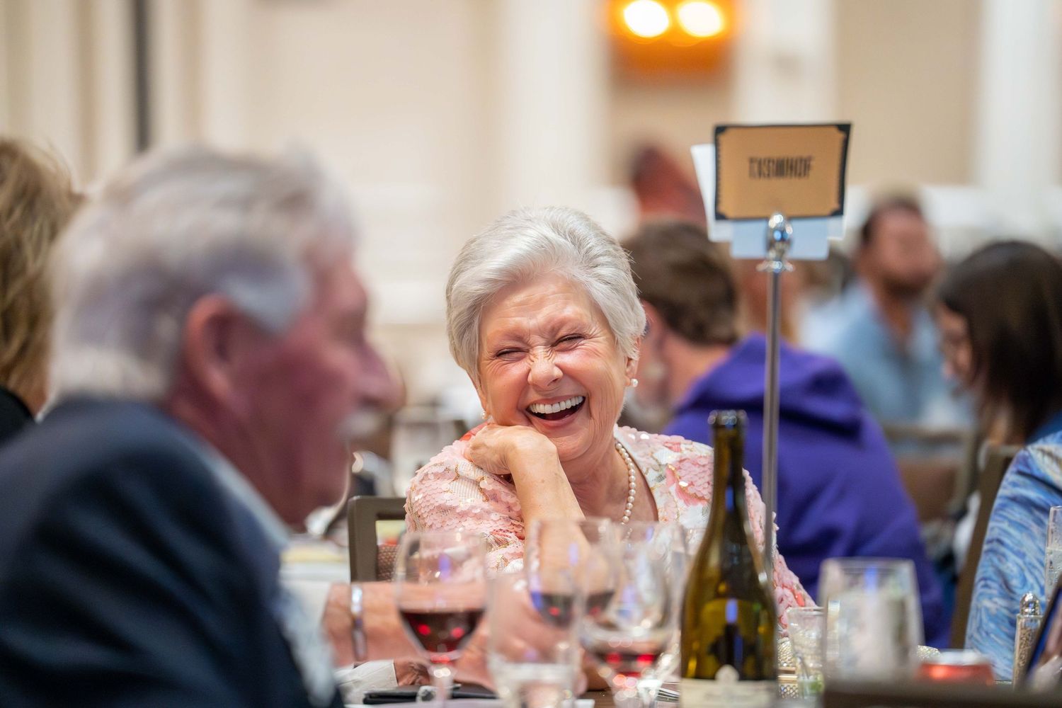 People enjoying wine and conversation at a dinner gathering with glasses and bottles on the table.