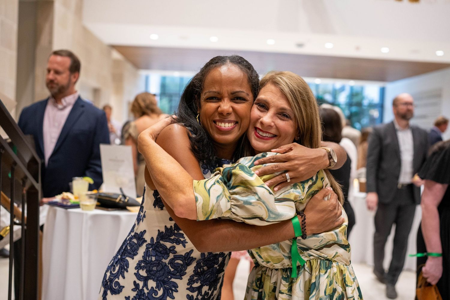 Attendees at a charity auction event smile and celebrate while holding up bid numbers in an indoor venue.