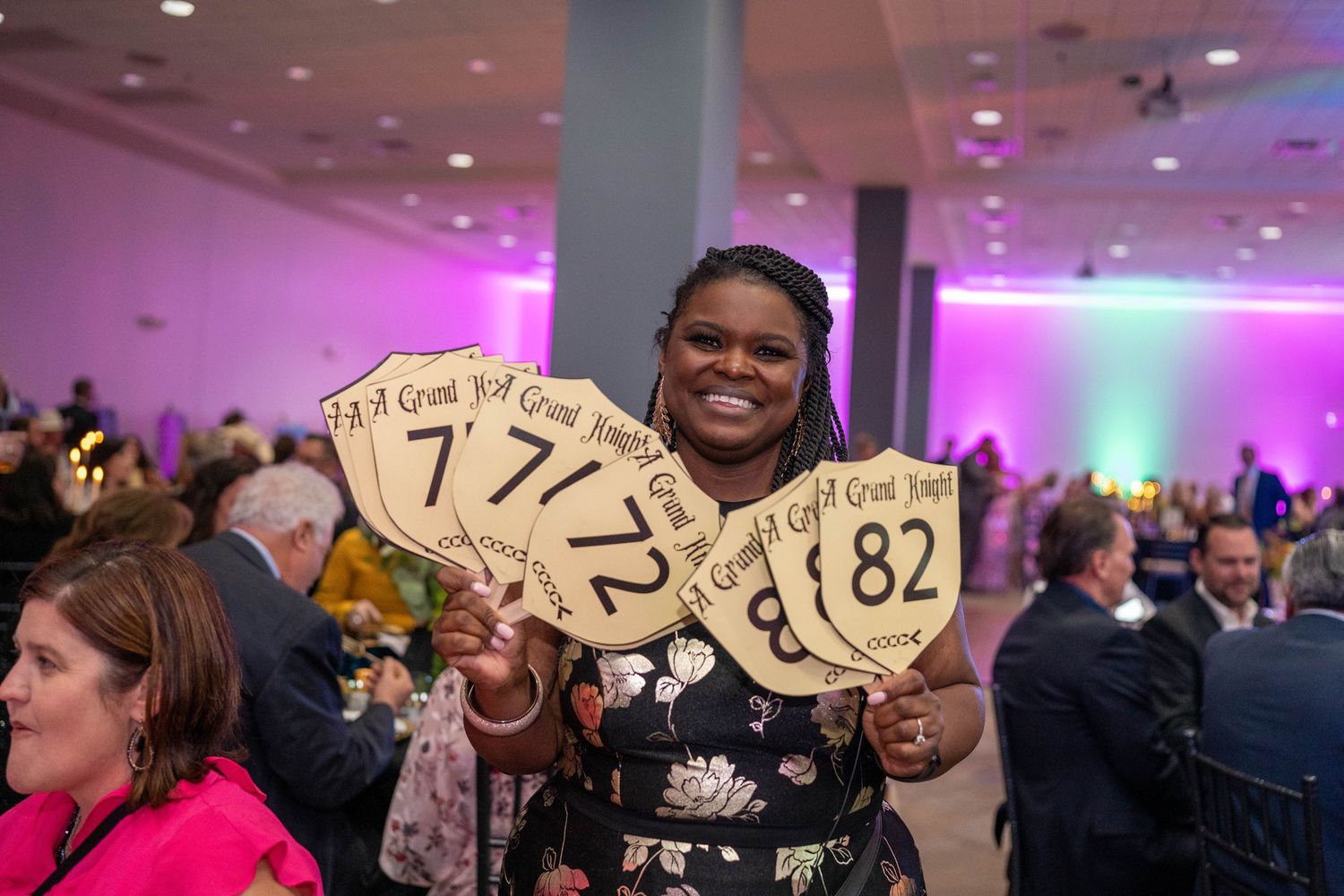 People hold up numbered auction paddles during a fundraising event with pink and blue lighting in the background.