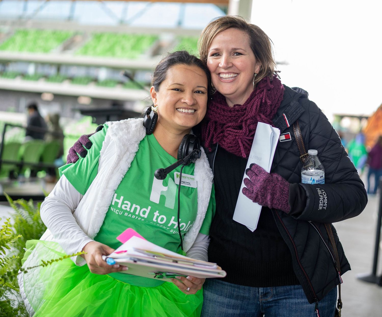 Volunteers in green tutus and aprons serve food at an outdoor community event.
