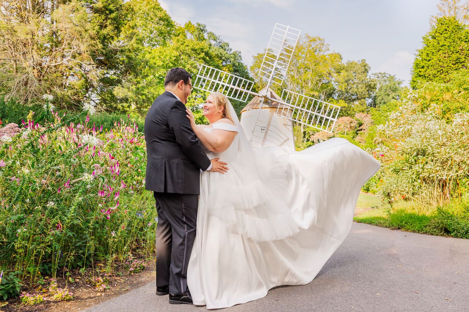 A couple shares a romantic moment on a garden path surrounded by lush greenery and blooming flowers.