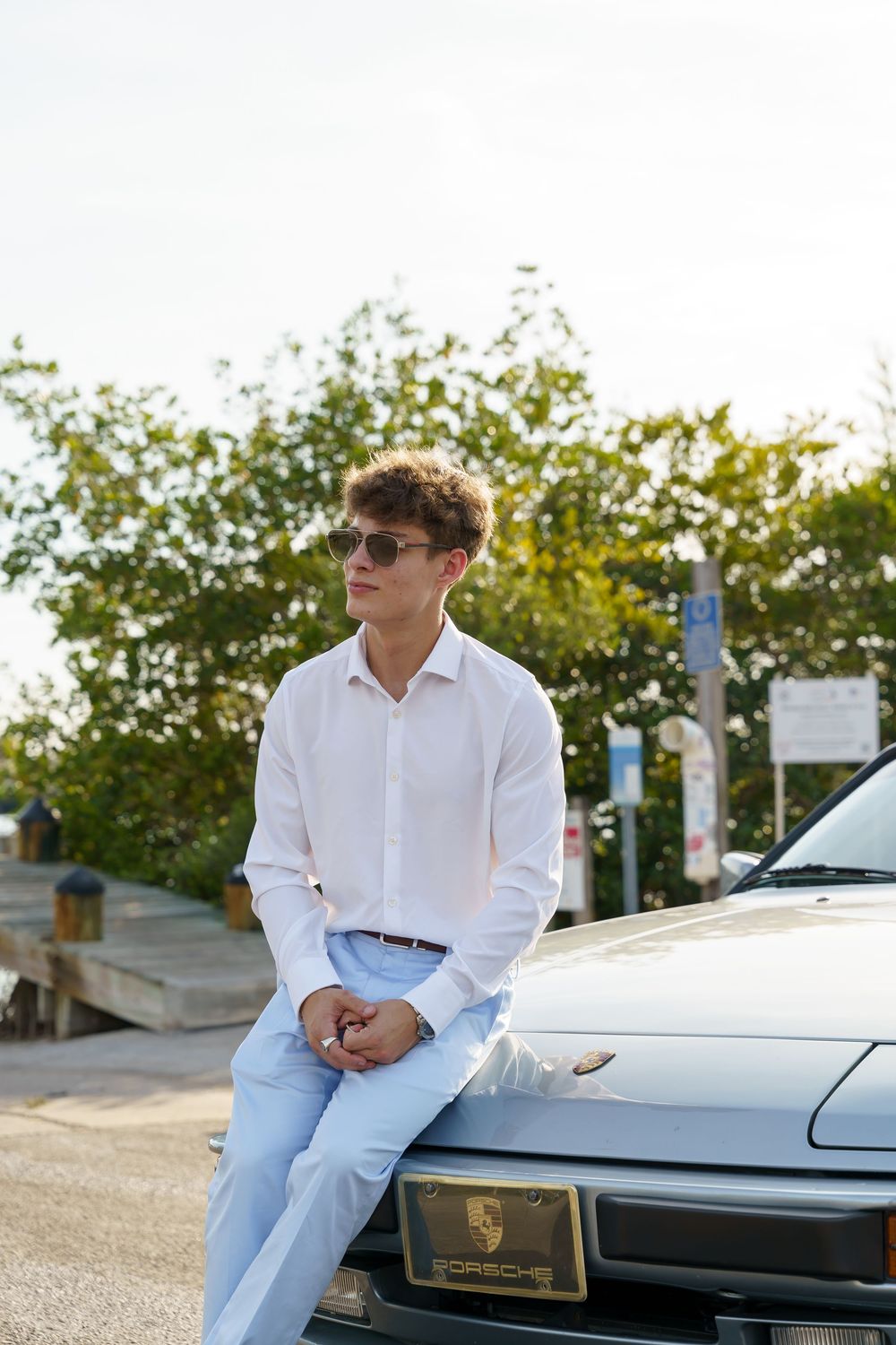 A sleek silver sports car photographed at sunset with lush greenery in the background.