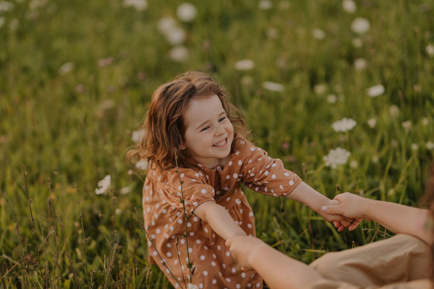 Person in floral dress plays joyfully in a summer meadow filled with wildflowers.