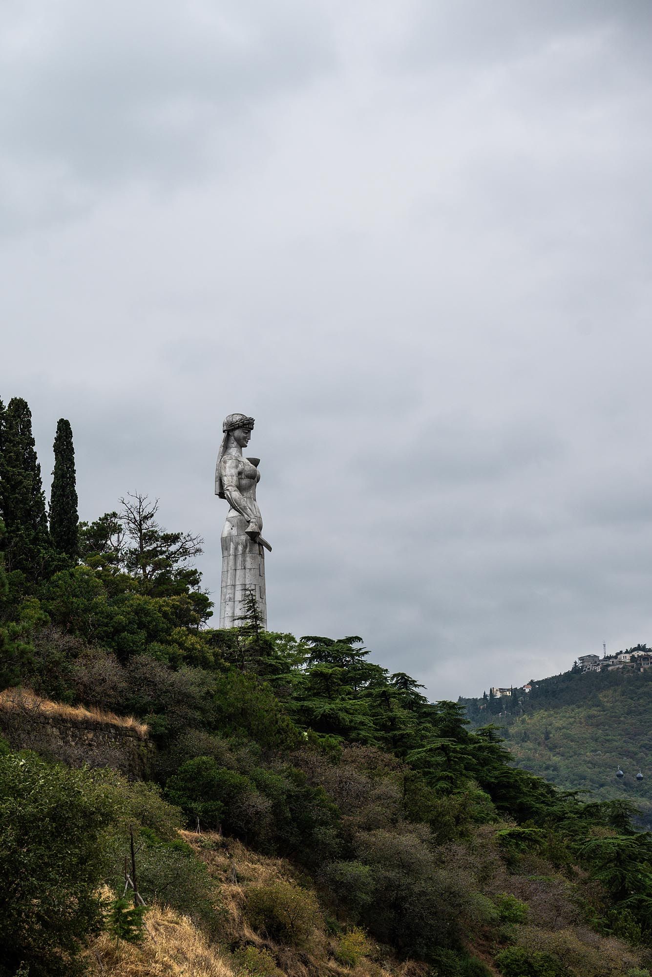 A large white statue stands atop a forested hill against a cloudy sky in a panoramic sequence of images.