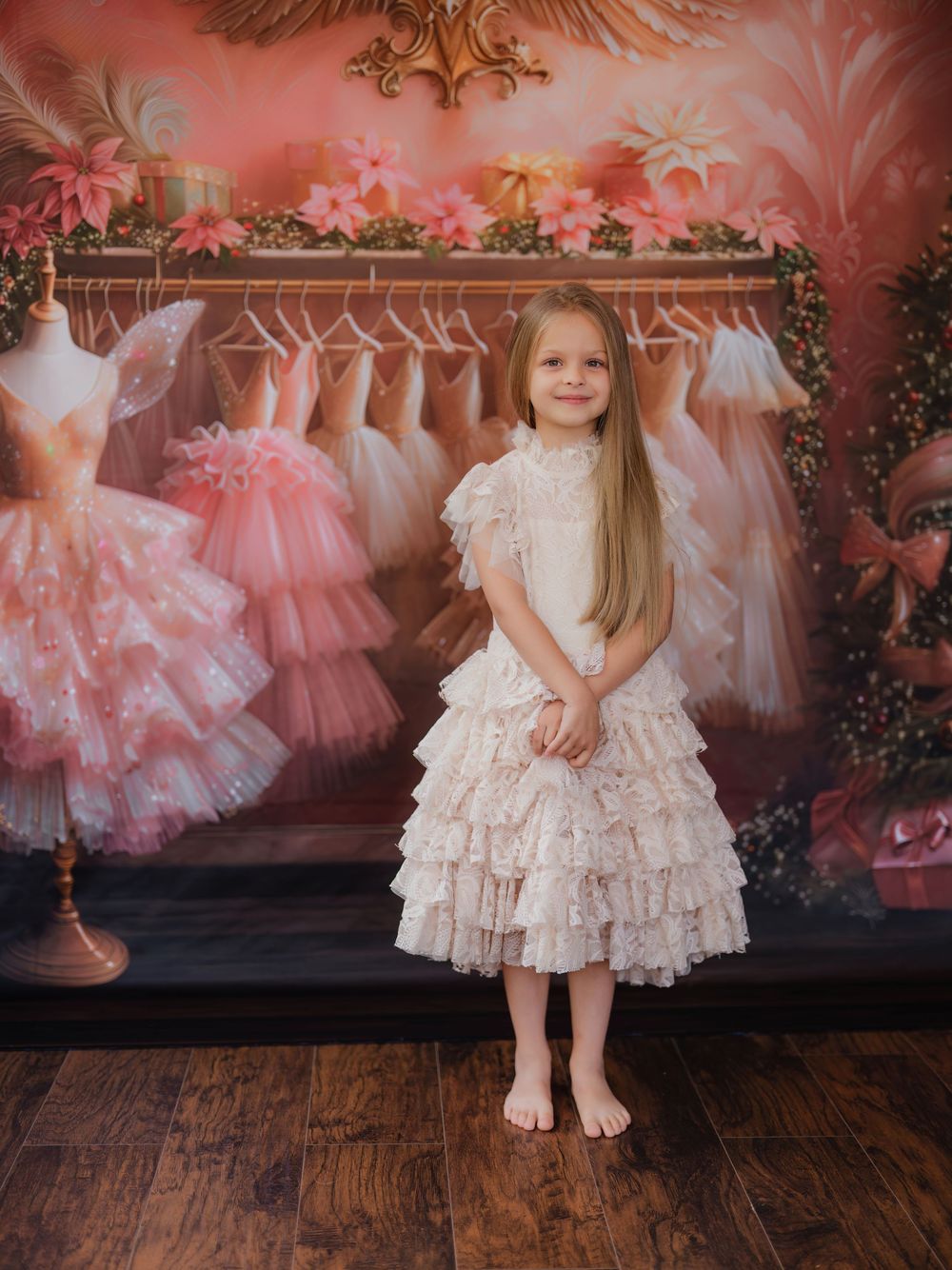 A series of pink tulle dresses hanging on a rack with a child in a white lace dress posing in front of them.
