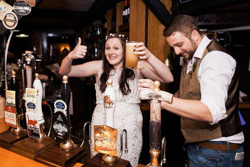 People enjoying drinks and socializing at a bar counter with beer taps and glassware visible in the background.
