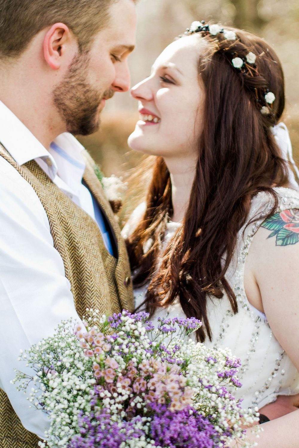 Romantic wedding couple embraces outdoors with purple wildflower bouquet and soft natural lighting.