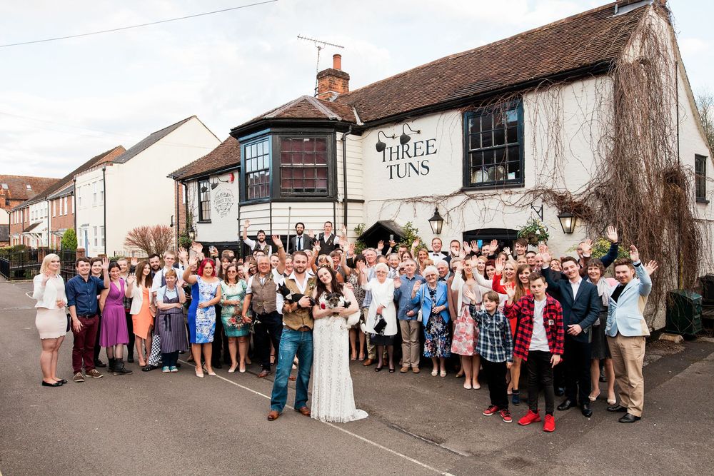 A group of people gathered outside a rustic building in what appears to be a wedding or social celebration.