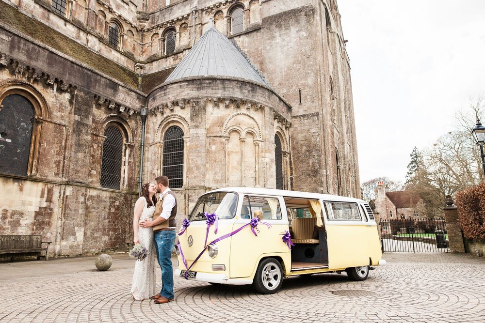 Vintage Volkswagen van parked in front of a historic stone church during a wedding photoshoot.