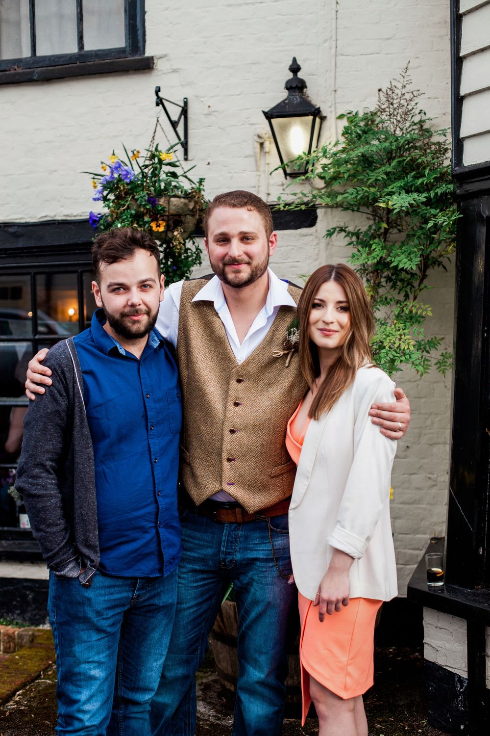 Three people standing together outside a building with white walls and black trim.