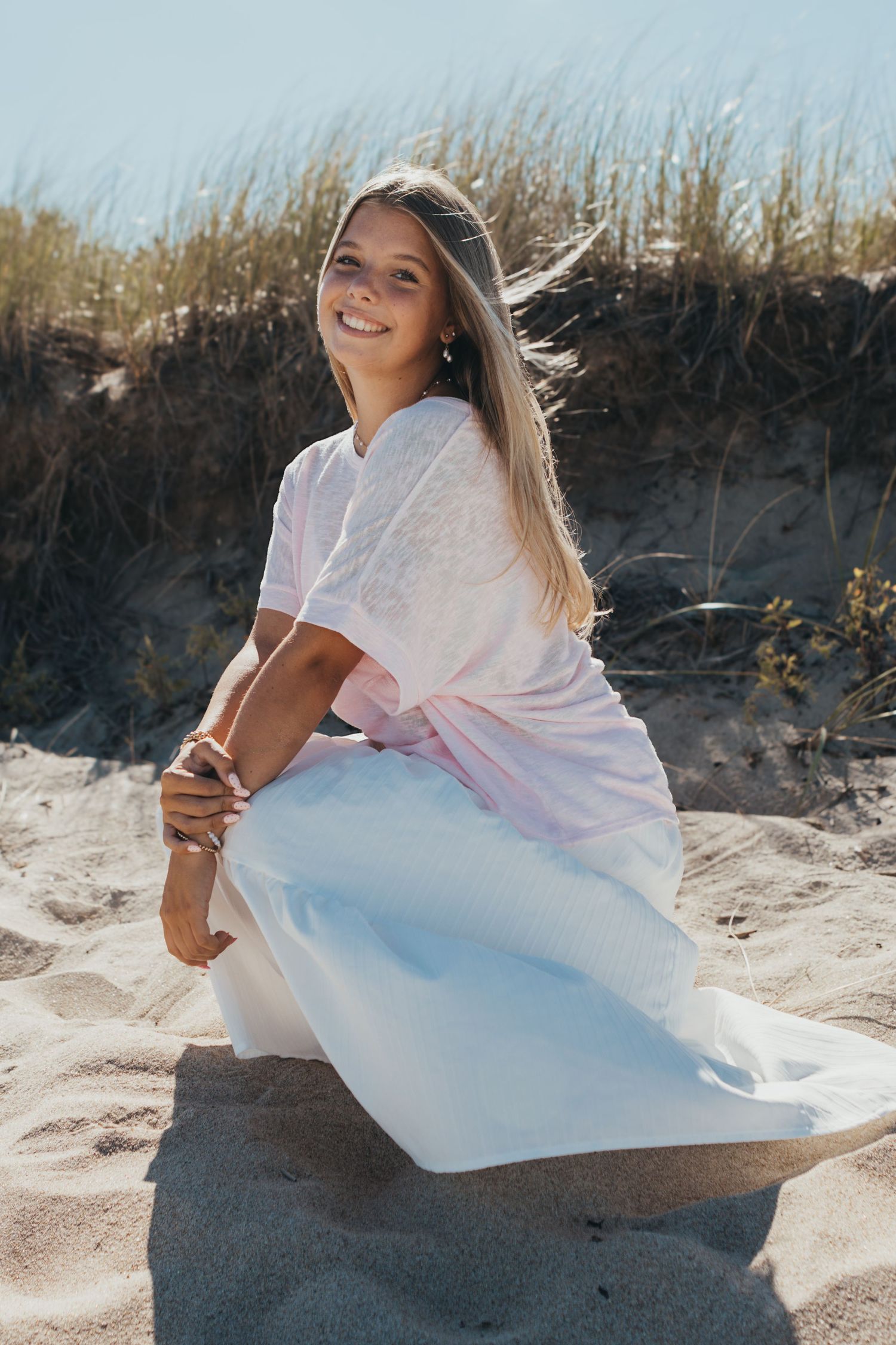 Casual beach photoshoot with flowing white outfit against sand dunes.