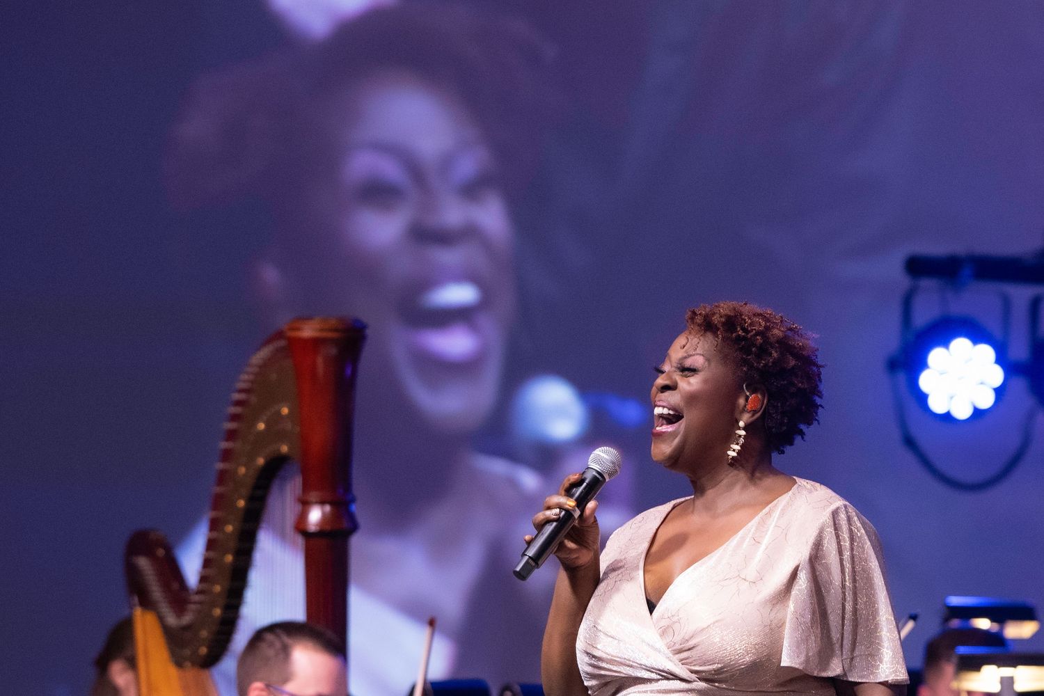 Female vocalist performing on stage with a harp and screen projection behind her.