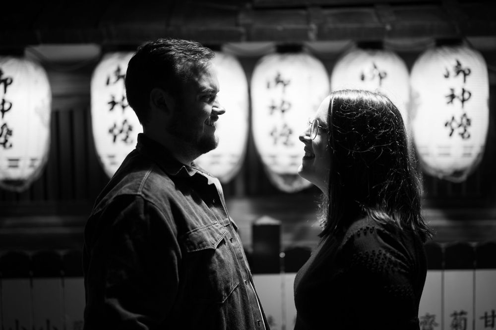 Black and white portrait of a couple facing each other with Japanese lanterns in the background.