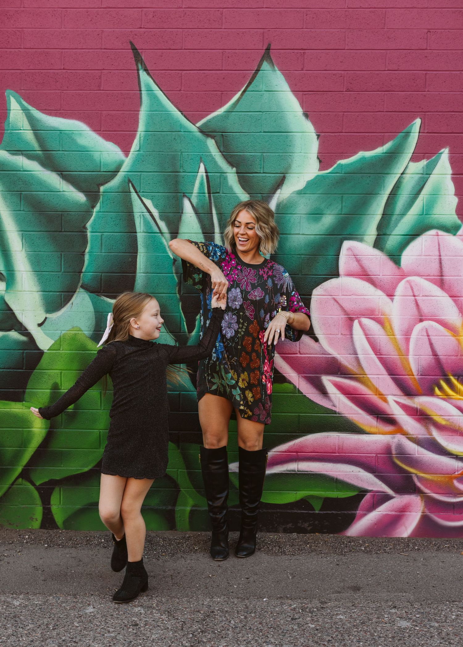 Dancing figures pose against a vibrant mural featuring pink flowers and green leaves.
