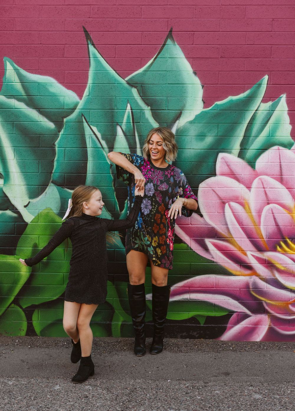 Dancing figures pose against a vibrant mural featuring pink flowers and green leaves.