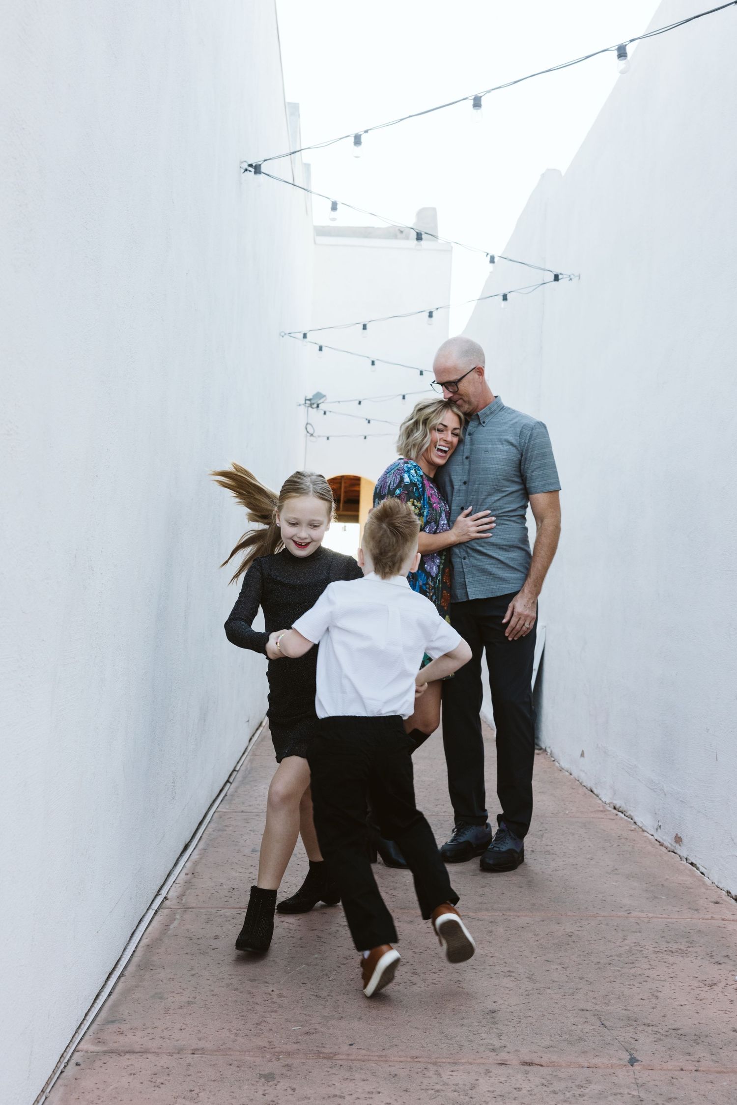 Playful dance sequence between family members in a white-walled corridor with string lights.