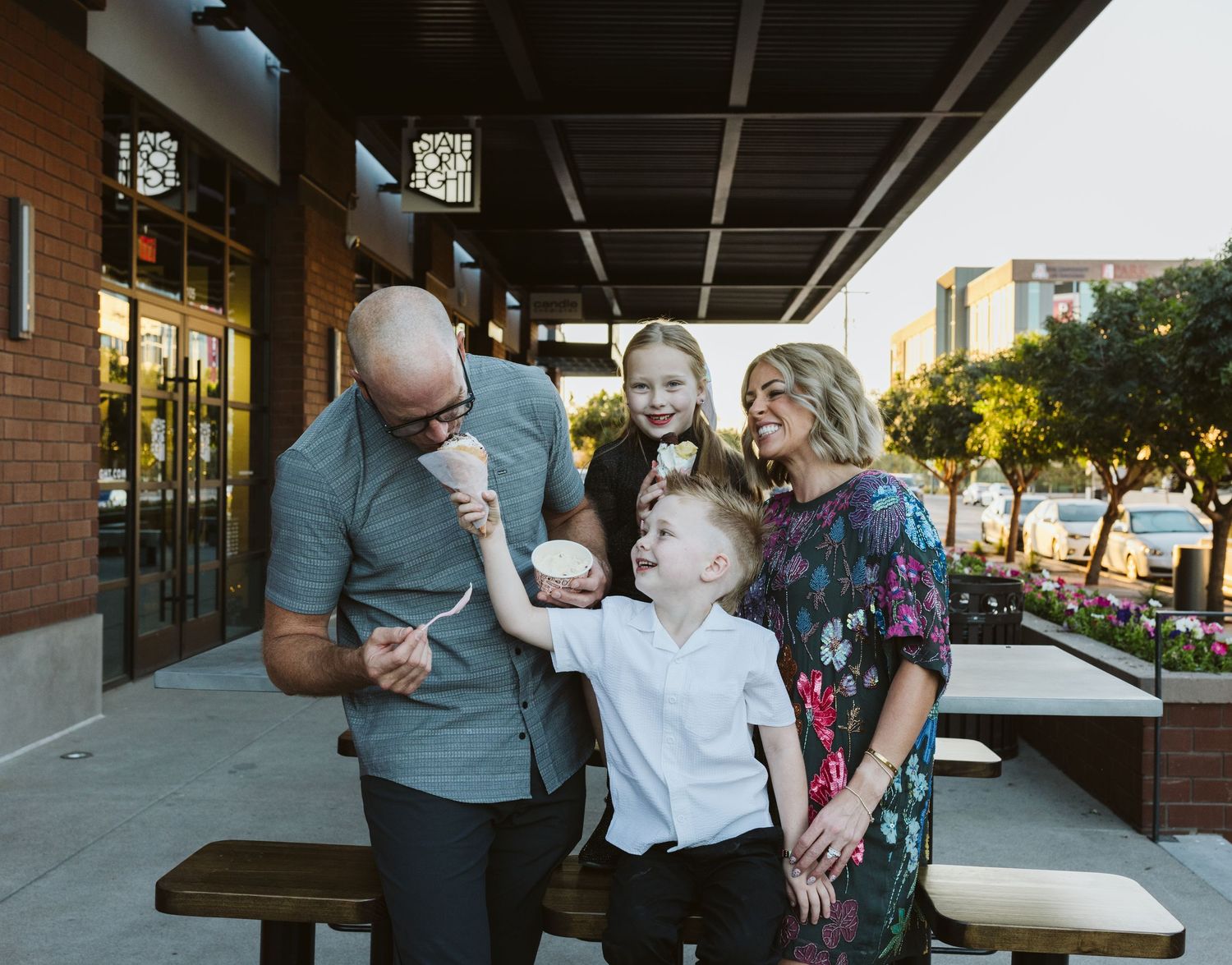 Family enjoying ice cream together at an outdoor picnic table on a sunny evening.