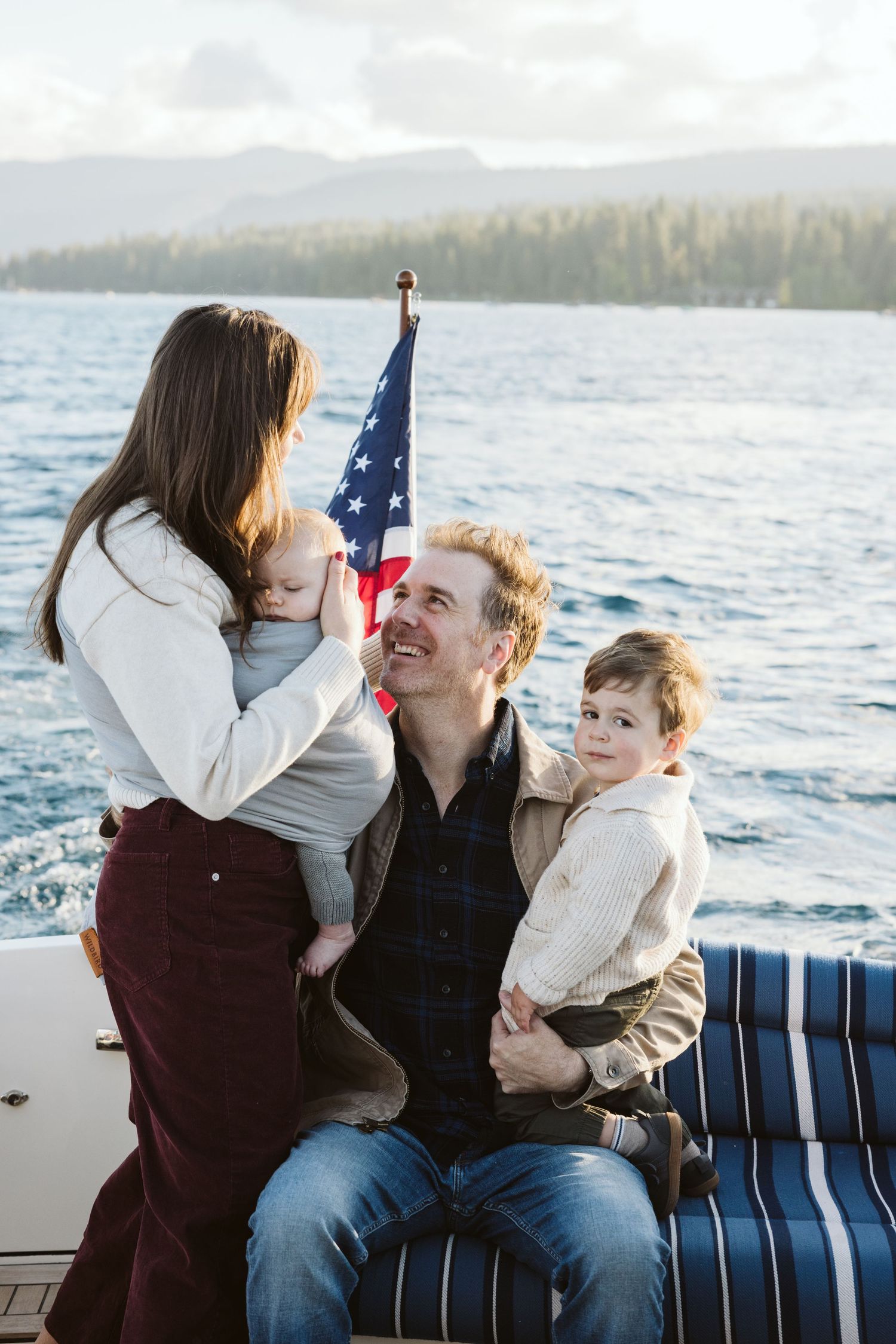 Family enjoying quality time on a boat with American flag and mountain backdrop.